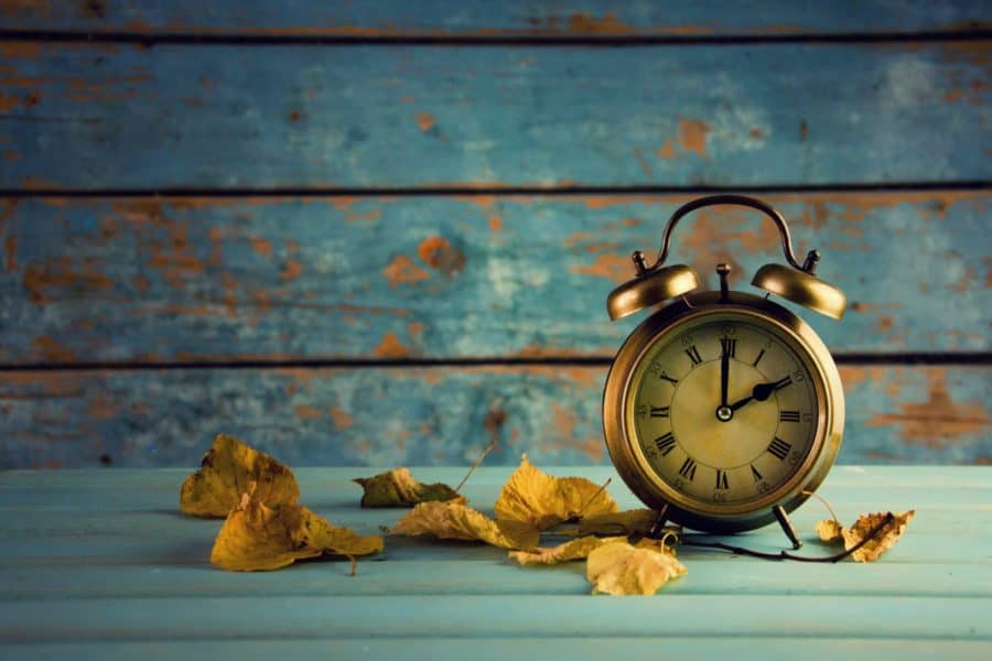 Golden vintage alarm clock with falling autumn leaves on a turquoise wooden surface, rustic background, symbolic of time and seasons, Greek City Times, aesthetic still life photography.