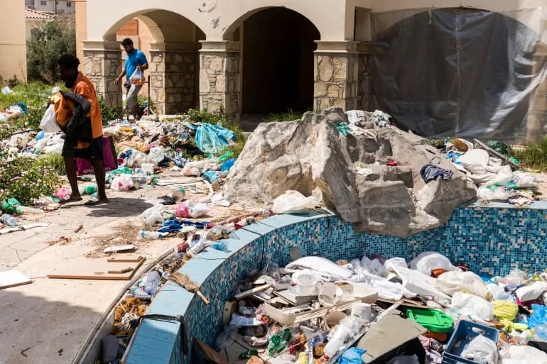Asylum seekers walk amid waste at the Ayios Nikolaos apartment complex, in Chloraka, a village of 7,000 people located on the outskirts of Paphos, Cyprus [Iakovos Hatzistavrou/AFP]
