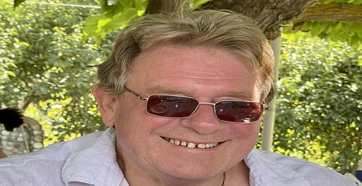 Author Peter Barber. Image of a sandyhaired man wearing a light blue shirt and sunglasses, smiling