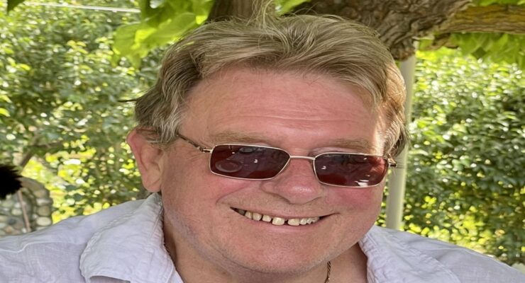 Author Peter Barber. Image of a sandyhaired man wearing a light blue shirt and sunglasses, smiling