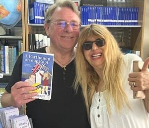 Author Peter Barber and his wife Alexandra. Image of a sandy color haired man wearing glasses and a black top holding up a book, the other arm around a woman with long blond hair wearing sunglasses and a while top
