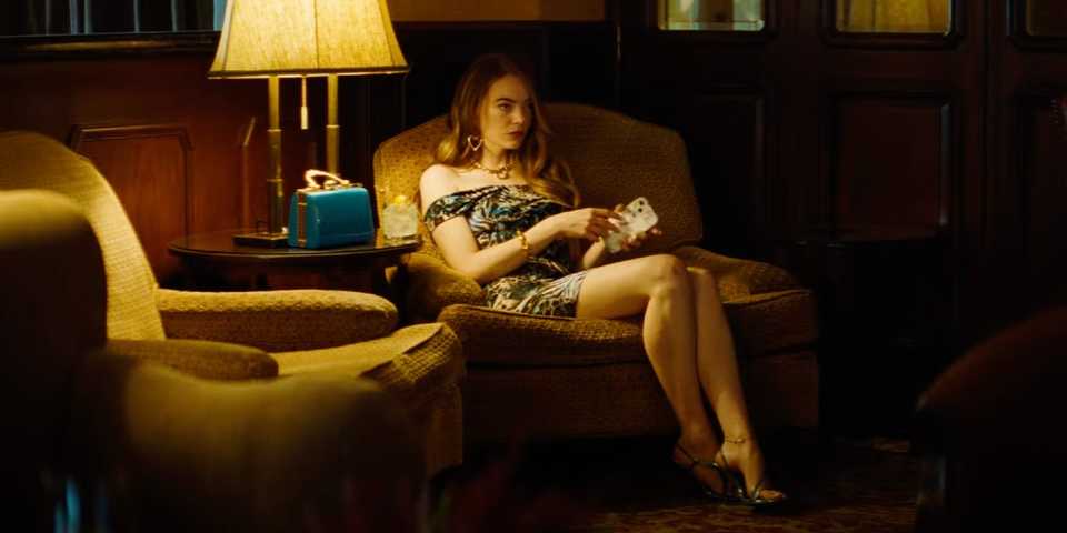 emma stone sitting in a chair in a dimly lit room in the kinds of kindness trailer