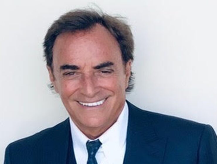 Actor Thaao Penghlis Cookbook Author Image by Thaao Penghlis. Image of a siling, tanned man with dark hair in a black suit, white short, and tie.
